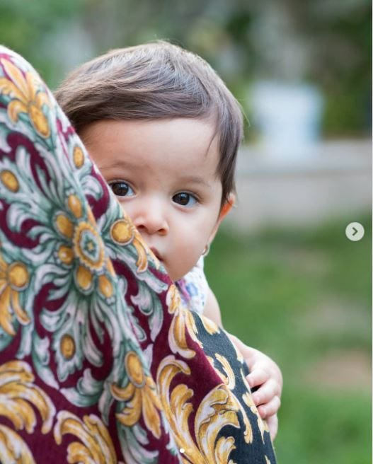 adorable little boy outdoors, peeping out from behind his mom's dress